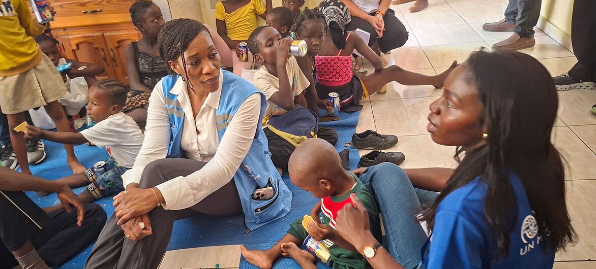 Edem Wosornu, Director of OCHA Crisis Response Division, sits on a blue mat with displaced women and children at a Community Resource Centre in Delmas, Haiti, supported by IOM.