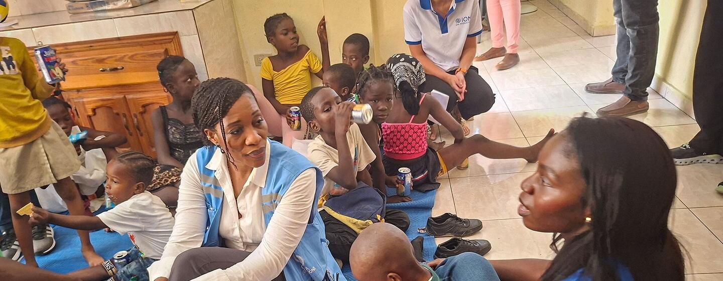 Edem Wosornu, directeur de la Division de la réponse aux crises de l'OCHA, est assis sur un tapis bleu avec des femmes et des enfants déplacés dans un centre de ressources communautaires à Delmas, en Haïti, soutenu par l'OIM.