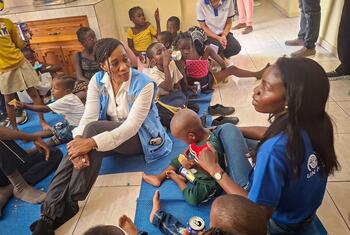 Edem Wosornu, Director of OCHA Crisis Response Division, sits on a blue mat with displaced women and children at a Community Resource Centre in Delmas, Haiti, supported by IOM.