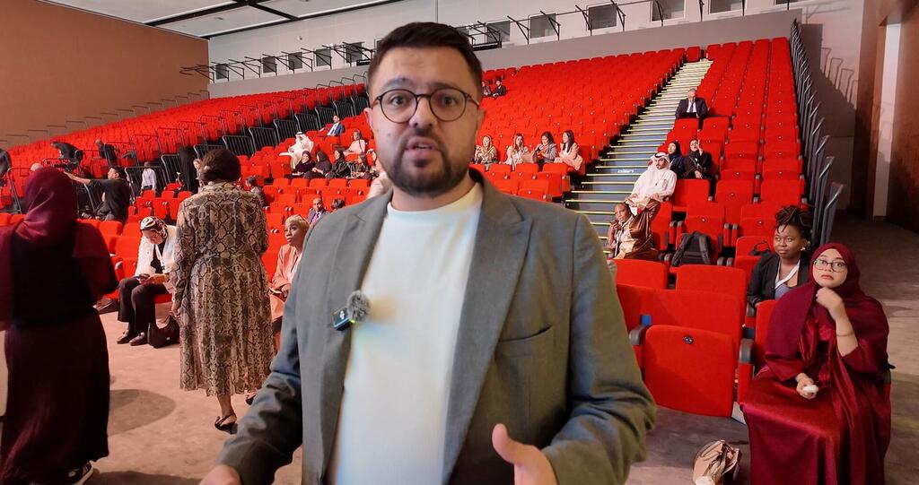 رجل يتحدث في مؤتمر في المنامة، البحرين، مع الجمهور الجالس على الكراسي الحمراء.