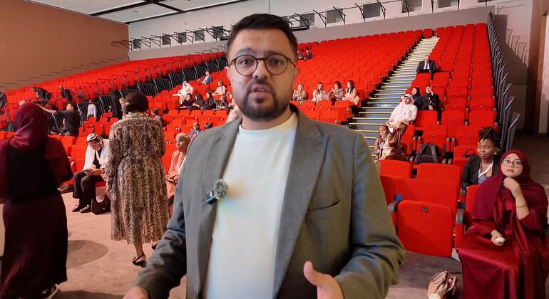 رجل يتحدث في مؤتمر في المنامة، البحرين، مع الجمهور الجالس على الكراسي الحمراء.