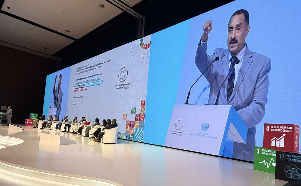 المتحدث، الذي تم تحديده باسم هاشم، يتحدث إلى الجمهور في منتدى استثمار رواد الأعمال العالمي 2026 في المنامة، البحرين، مع شاشة كبيرة تعرض صورته وموضوع الحدث.