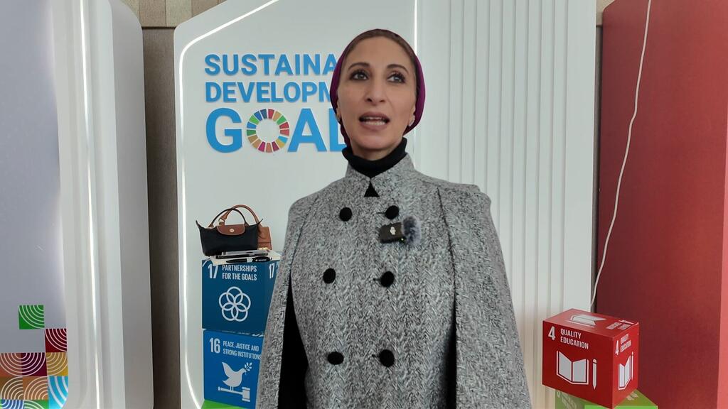 Dina Najar, UN News reporter, stands in front of a backdrop displaying Sustainable Development Goals, specifically SDG 4 (Quality Education), SDG 16 (Peace, Justice, and Strong Institutions), and SDG 17 (Partnerships for the Goals), at the WEIF2026 event in Manama, Bahrain.