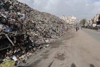 Une grande pile de déchets se dresse dans une rue du marché de Firas, dans la ville de Gaza, avec des gens qui marchent à distance alors que le PNUD et les organisations locales commencent les efforts de nettoyage.