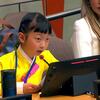 A young girl named Emma Lee, wearing a yellow traditional outfit, speaks into a microphone at a UN conference, with a nameplate in front of her.