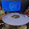 Wanawake weusi wawili wameketi kwenye meza ya mviringo yenye maikrofoni katika studio ya utangazaji, wakiwa na skrini kubwa inayoonyesha nembo ya Umoja wa Mataifa nyuma yao.