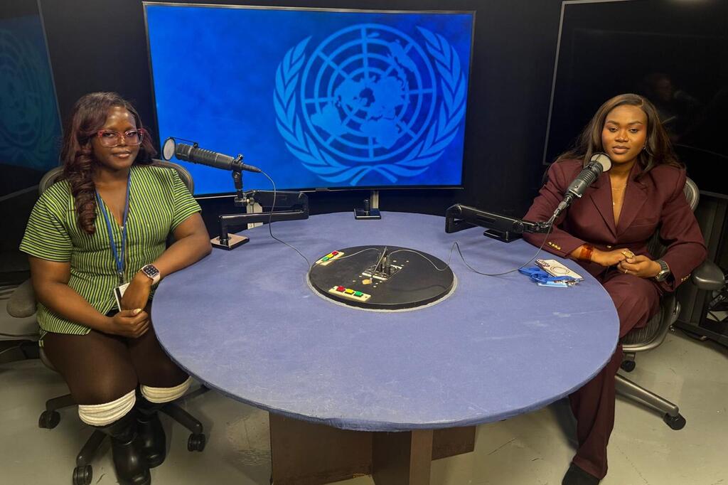 Wanawake weusi wawili wameketi kwenye meza ya mviringo yenye maikrofoni katika studio ya utangazaji, wakiwa na skrini kubwa inayoonyesha nembo ya Umoja wa Mataifa nyuma yao.