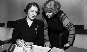 Picha nyeusi na nyeupe ya wanawake wawili, waliotambuliwa kama Dorothy Hodgkin na Eleanor Roosevelt, wakitazama nyaraka kwenye meza ya mkutano na nembo ya Umoja wa Mataifa ikionekana kwenye ukuta nyuma yao.