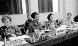 Picha nyeusi na nyeupe ya wanawake kwenye meza rasmi ya mkutano huko Geneva, ikiwa ni pamoja na Eugenia Charles, pamoja na ishara za 'Wakilishi wa Katibu Mkuu wa Umoja wa Mataifa' na 'Rais'.
