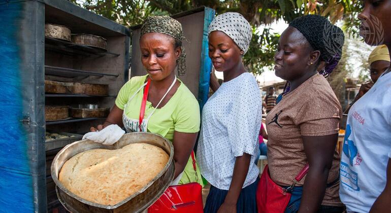 Kikundi cha wanawake wa Kiafrika nchini Liberia, mmoja akishikilia keki yenye umbo la moyo iliyotoka kwenye oveni, wakionyesha ustadi wao wa kuoka na ujasiriamali wa jamii.