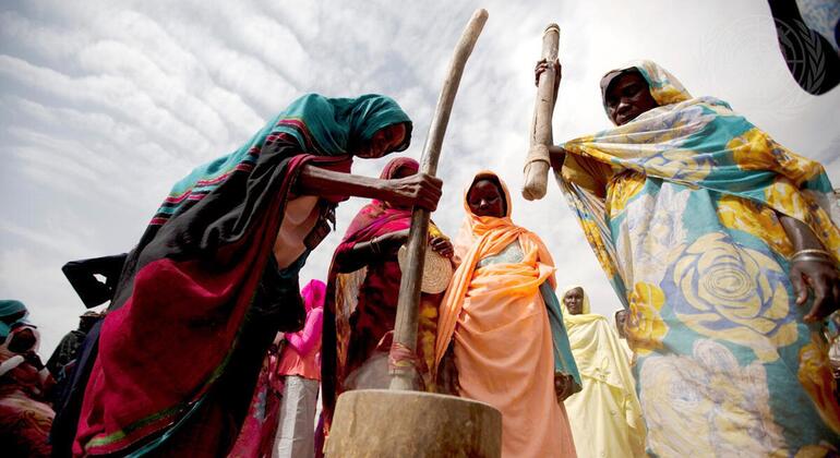 Wanawake wenye mavazi ya kitamaduni yenye rangi mbalimbali hutumia pishi kubwa za mbao kusaga nafaka katika chokaa huko Darfur, Sudan.