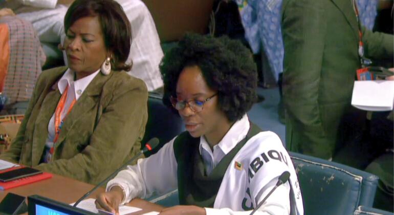 Duas mulheres africanas representando Moçambique em uma conferência internacional. A mulher em primeiro plano está escrevendo enquanto a mulher em segundo plano está assistindo. Uma placa azul com "MOZAMBIQUE" é visível na mesa.