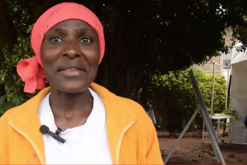 Mwanamke wa Kenya akiwa amevaa shufu ya rangi ya waridi na koti la manjano anaongea wakati wa mahojiano nje.