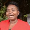 Mwanamke mweusi aliyevaa koti jekundu anaongea wakati wa mahojiano ya nje mbele ya alama ya Angelica's Home huko Kajiado, Kenya.