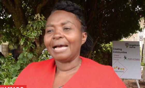 Mwanamke mweusi aliyevaa koti jekundu anaongea wakati wa mahojiano ya nje mbele ya alama ya Angelica's Home huko Kajiado, Kenya.