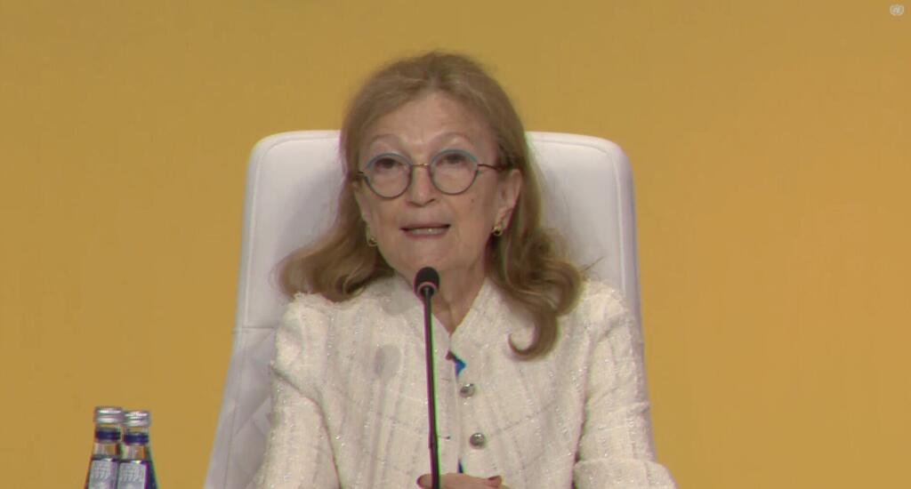 诺拉·卢斯蒂格 (Nora Lustig),一位老年女性,头发金发,眼镜,穿着白色克,在小组讨论会上用麦克风说话.