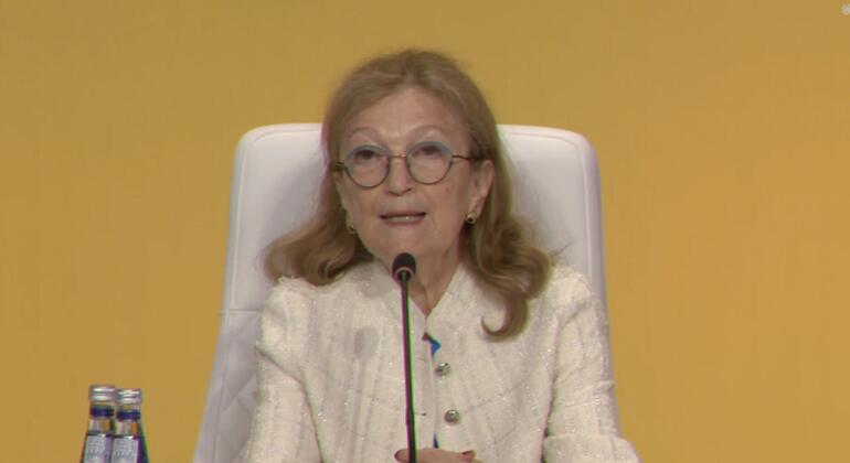 诺拉·卢斯蒂格 (Nora Lustig),一位老年女性,头发金发,眼镜,穿着白色克,在小组讨论会上用麦克风说话.