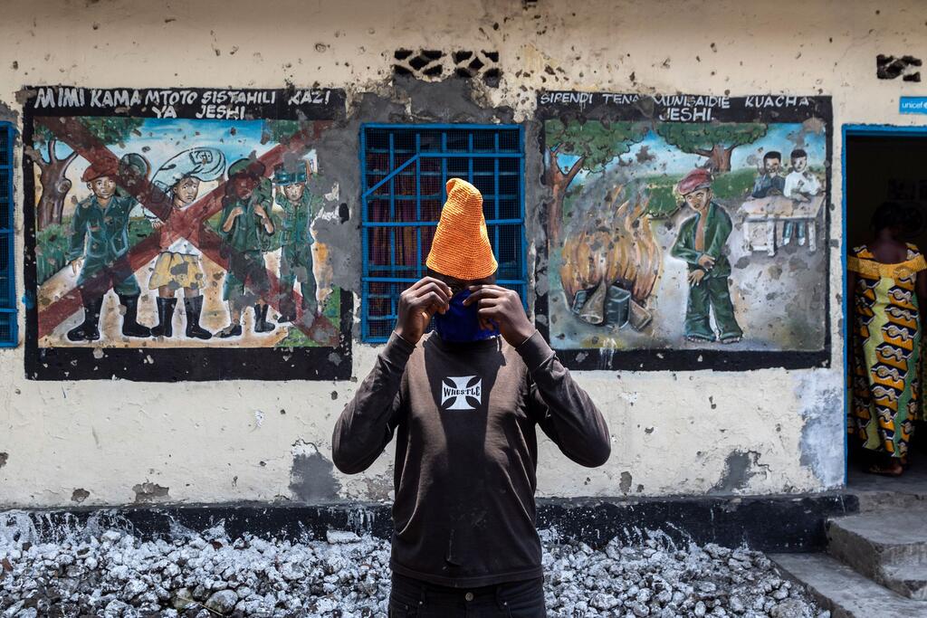 شاب يقوم بتعديل قناع الوجه بينما يقف أمام اللوحات الجدارية التي تصور إزالة الحركة في مركز عبور للأطفال مدعوم من اليونيسيف في جوما، جمهورية الكونغو الديمقراطية.