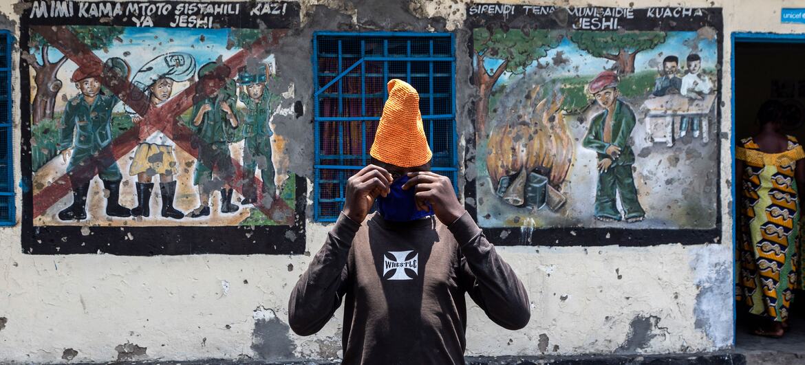 Um jovem ajusta uma máscara de rosto enquanto fica em frente a murais que retratam a desmobilização em um centro de trânsito para crianças apoiado pela UNICEF em Goma, RDC.