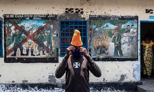 A young person adjusts a face mask while standing in front of murals depicting de-mobilization at a UNICEF-supported transit center for children in Goma, DRC.