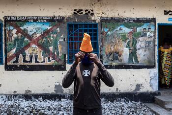A young person adjusts a face mask while standing in front of murals depicting de-mobilization at a UNICEF-supported transit center for children in Goma, DRC.
