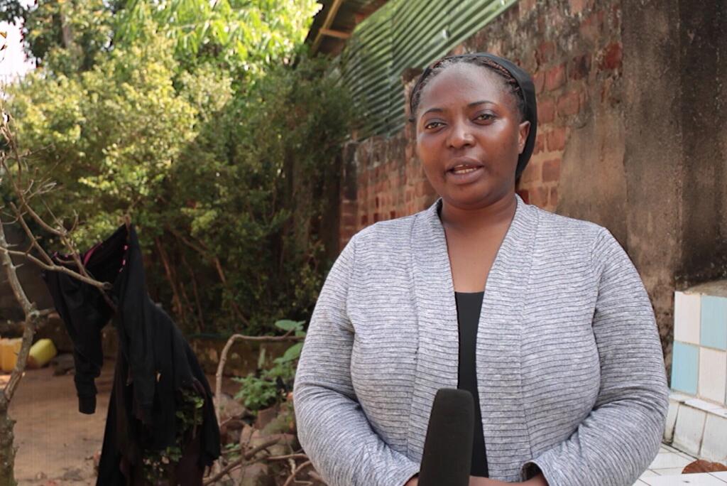 Mwanamke katika cardigan ya kijivu akibeba kipaza sauti wakati wa mahojiano ya nje kwa ajili ya Siku ya Redio katika Jamhuri ya Kidemokrasia ya Kongo.