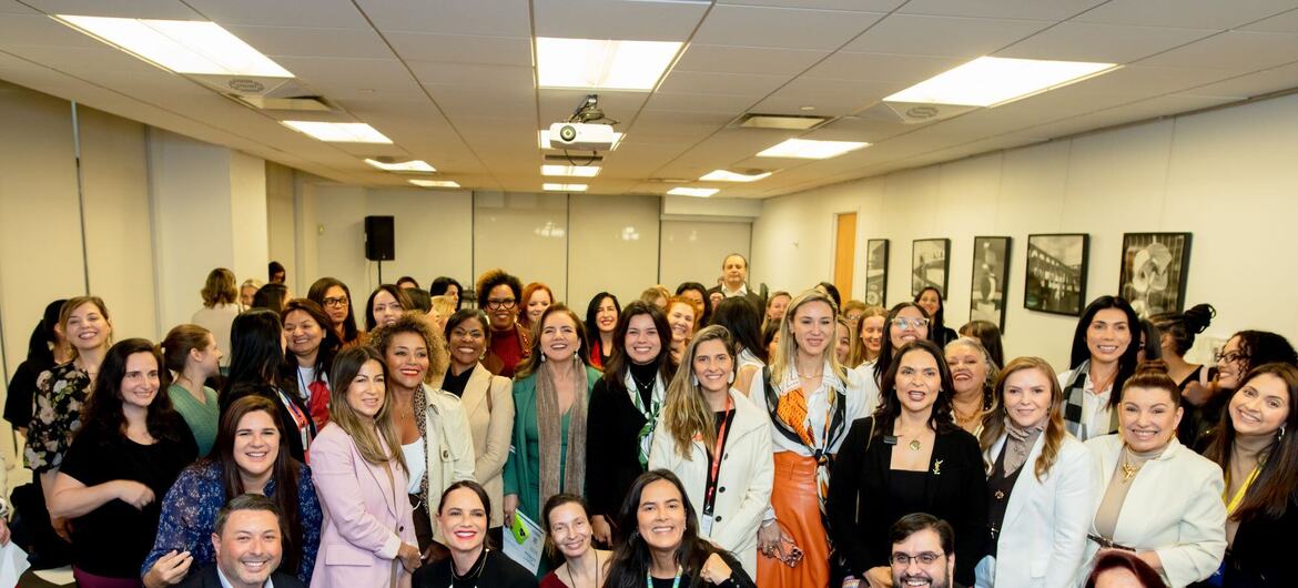 Um grande grupo de profissionais sorridentes, principalmente mulheres, posando para uma foto de grupo em uma conferência ou evento no Brasil.