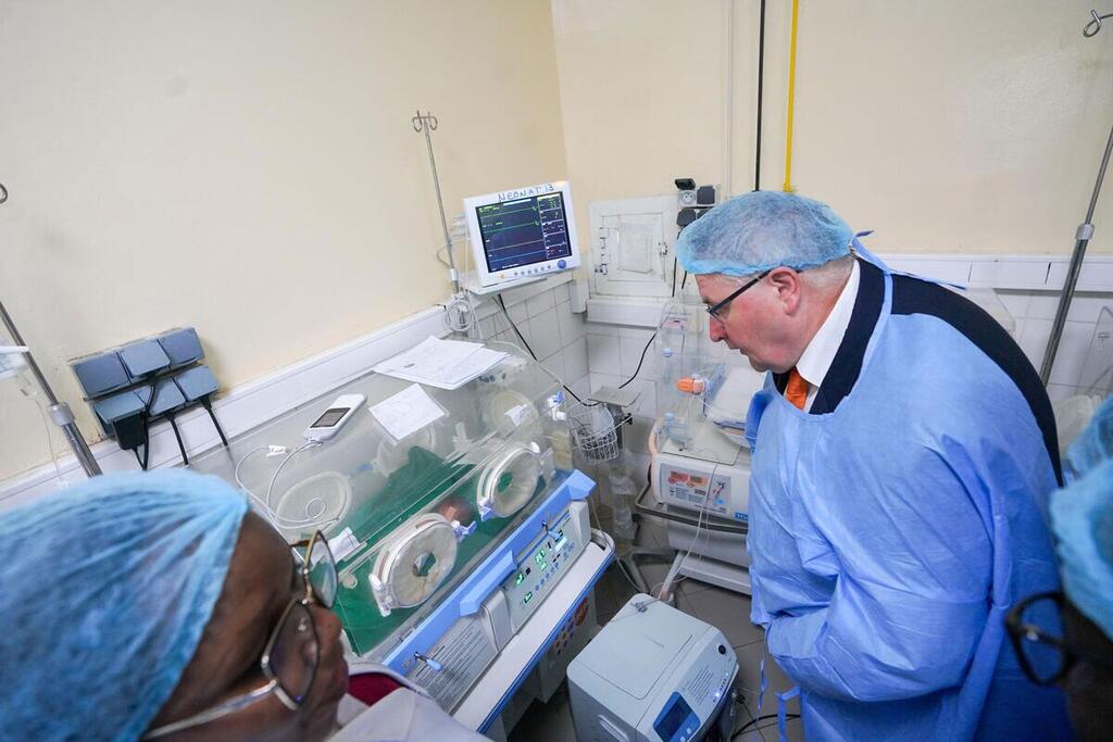 UNFPA Deputy Executive Director Andrew Saberton wearing medical scrubs and a hairnet looks at an incubator in a hospital maternity ward in Chad.