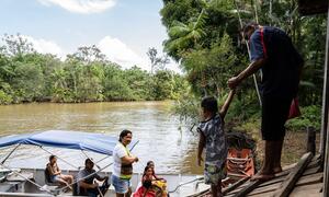 Afisa wa Afya ya Jamii Dene Maria Rodrigues André anamsaidia mvulana mdogo kupanda mashua kwenye Mto Caripetuba huko Abaetetuba, Pará, Brazili, pamoja na familia ya Pinheiro.