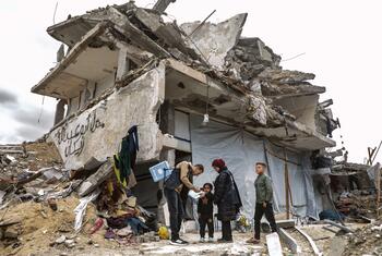 A health worker administers a polio vaccine to a child in front of a damaged building in Jabalia, Gaza, as part of a vaccination campaign.