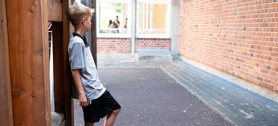 A young boy in a grey shirt and black shorts leans against a wooden structure on a playground at Gartenstadt Primary School in Cologne-Longerich.