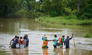 Wafanyakazi wa afya wanapita kwenye mto uliofurika kaskazini mwa Ghana wakiwa wamebeba vifaa vya chanjo.