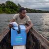 Laha Elersene Razafimahavory sostiene una caja de refrigeración azul de vacunas de UNICEF mientras se sienta en una piragua de madera en un río de Madagascar.