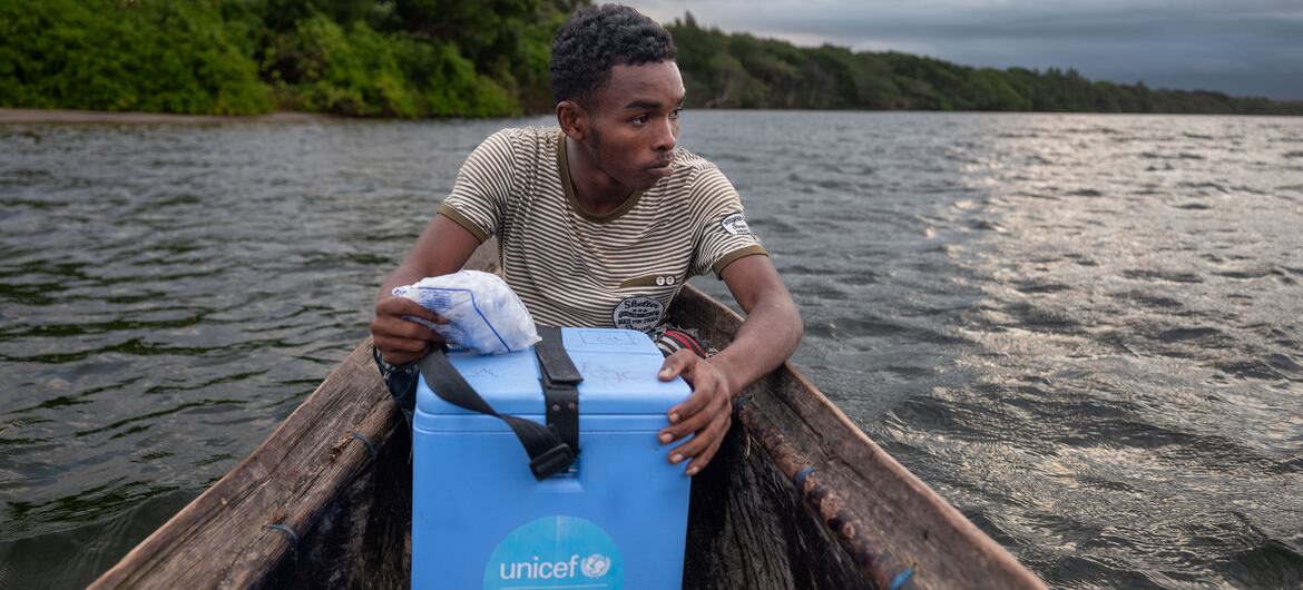 Laha Elersene Razafimahavory sostiene una caja de refrigeración azul de vacunas de UNICEF mientras se sienta en una piragua de madera en un río de Madagascar.