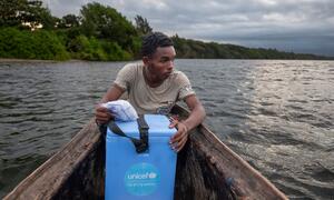 Laha Elersene Razafimahavory anashikilia sanduku la baridi la UNICEF la rangi ya bluu la chanjo akiwa ameketi kwenye mtumbwi wa mbao kwenye mto nchini Madagaska.