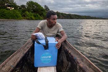 Laha Elersene Razafimahavory sostiene una caja de refrigeración azul de vacunas de UNICEF mientras se sienta en una piragua de madera en un río de Madagascar.