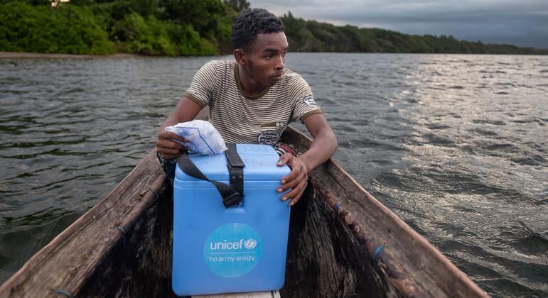 Laha Elersene Razafimahavory sostiene una caja de refrigeración azul de vacunas de UNICEF mientras se sienta en una piragua de madera en un río de Madagascar.