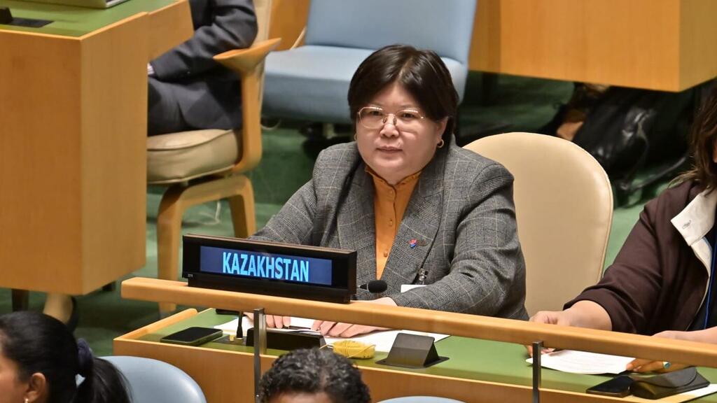 Эльвира Азимова, представительница Казахстана, сидит за столом конференции с табличкой "KAZAKHSTAN" перед собой.