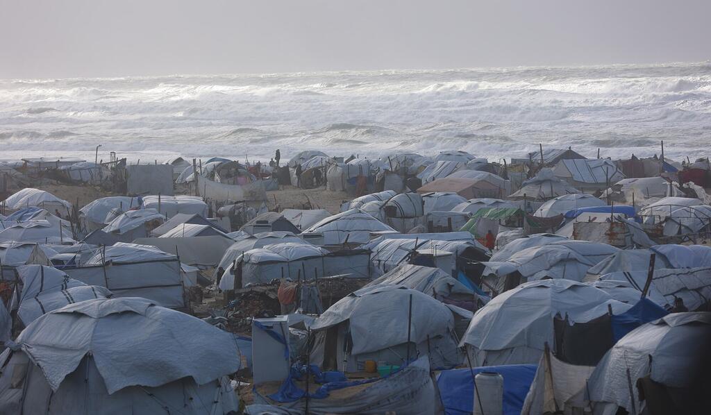 Un campamento de refugiados lleno de gente en Gaza con numerosas carpas improvisadas a lo largo de la costa, con olas que chocan en el fondo.