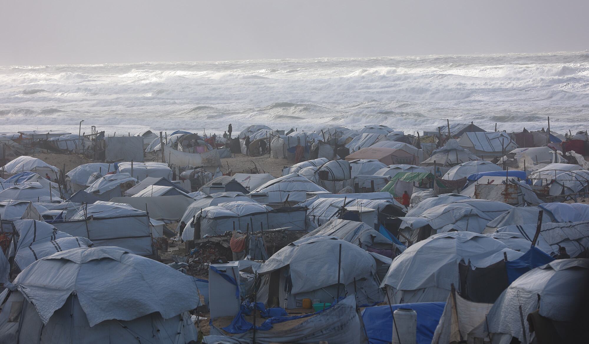 Un camp de réfugiés bondé à Gaza avec de nombreuses tentes improvisées le long de la côte, les vagues s'écrasant en arrière-plan.