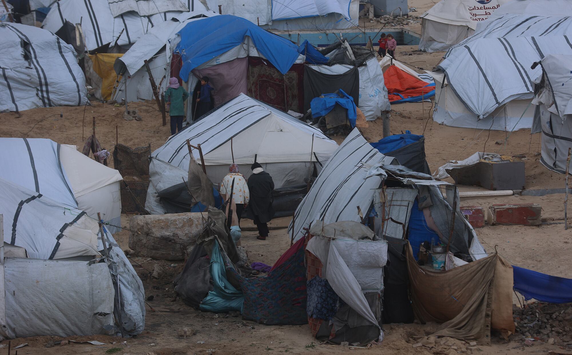 Les gens traversent un camp de réfugiés improvisé à Gaza, entouré de tentes et d'abris rudimentaires.
