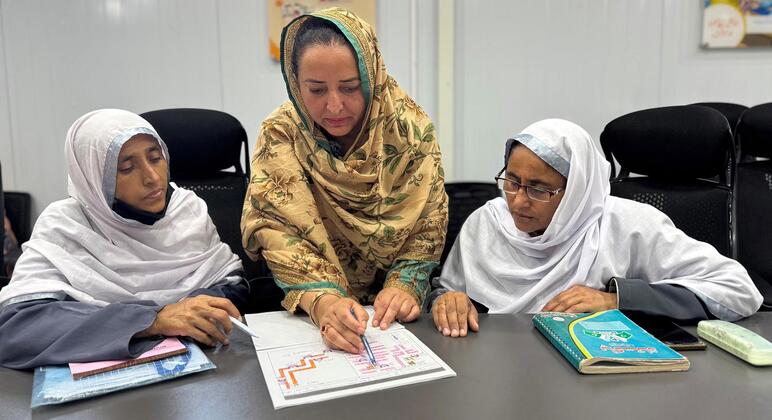 Три женщины-здравоохранители в Пакистане, обученные ВОЗ, просматривают записи о вакцинации и диаграммы во время кампании по профилактике рака шейки матки.