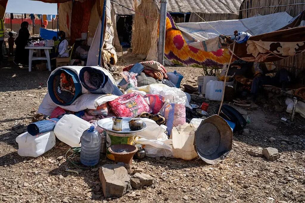Une vue des conditions de vie dans le camp de déplacés d'Abu Al Naja au Soudan, montrant une pile de fournitures d'aide humanitaire, y compris des conteneurs d'eau, des couvertures et des sacs alimentaires, devant des abris de fortune.