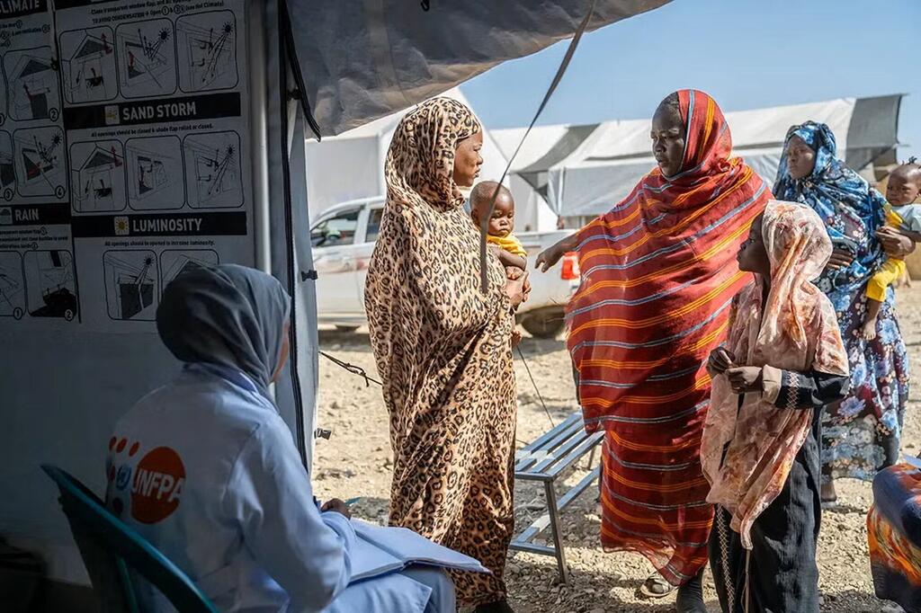 عامل إغاثة تابع لصندوق الأمم المتحدة للسكان يتفاعل مع مجموعة من النساء والأطفال السودانيين في مخيم للنازحين داخلياً.