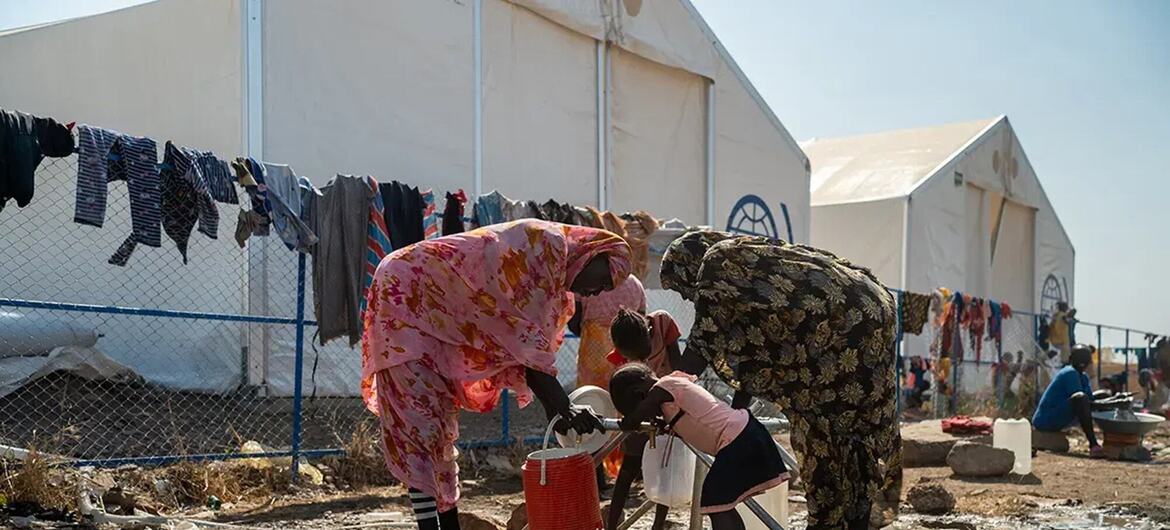 Des femmes et des enfants ramassant de l'eau dans un camp de réfugiés boueux au Soudan.