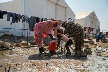 Des femmes et des enfants ramassant de l'eau dans un camp de réfugiés boueux au Soudan.