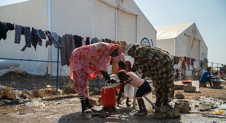 Des femmes et des enfants ramassant de l'eau dans un camp de réfugiés boueux au Soudan.