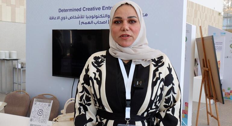 امرأة ترتدي حجابًا وملابس مصممة تقف أمام خلفية مكتوب عليها "ريادة الأعمال الإبداعية المحددة" في حدث في المنامة، البحرين، لتعزيز تمكين المرأة وريادة الأعمال الإبداعية.