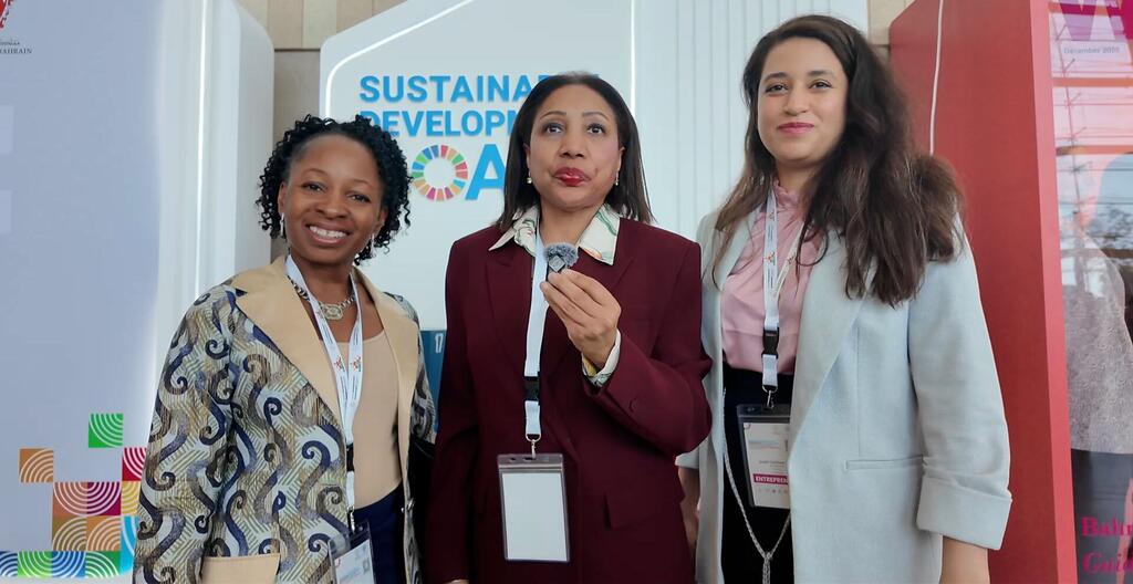 Wanawake watatu wenye mavazi ya kitaalamu wakiwa wamesimama pamoja katika tukio la Malengo ya Maendeleo Endelevu huko Manama, Bahrain, wakiwakilisha uwezo wa wanawake na ujasiriamali.