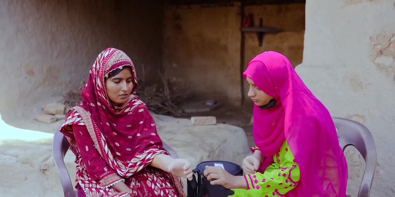 روایتی لباس میں دو خواتین پاکستان میں ایک دیہی ماحول میں ایک مصنوعی آلہ کے ساتھ بات چیت کرتی ہیں ، جو بیونکس اور اقوام متحدہ کی خواتین کے مابین ایک پائلٹ تعاون کا حصہ ہے۔